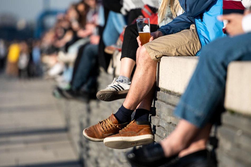 Menschen sitzen auf einer Mauer am Rheinboulevard und genießen die Sonne