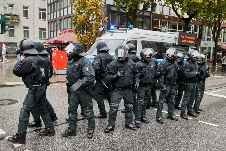 Polizisten mit Helmen stehen in St. Georg vor einem Einsatzwagen mit der Aufschrift "Ihre Versammlung wurde verboten".