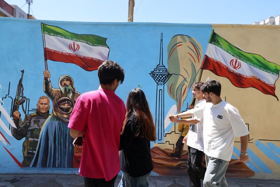 Iranians walk past an anti-US and anti-Israel mural painted on a wall in the capital of Tehran on May 10, 2026.
