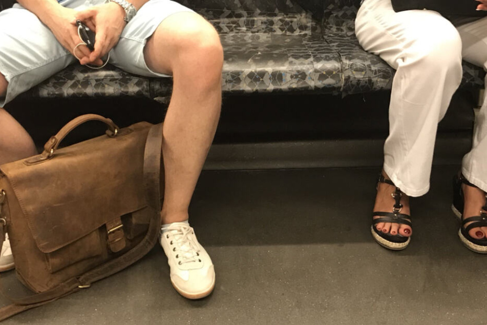 Ein Mann sitzt breitbeinig in der U-Bahn, während sich die Frau von ihm weglehnt.
