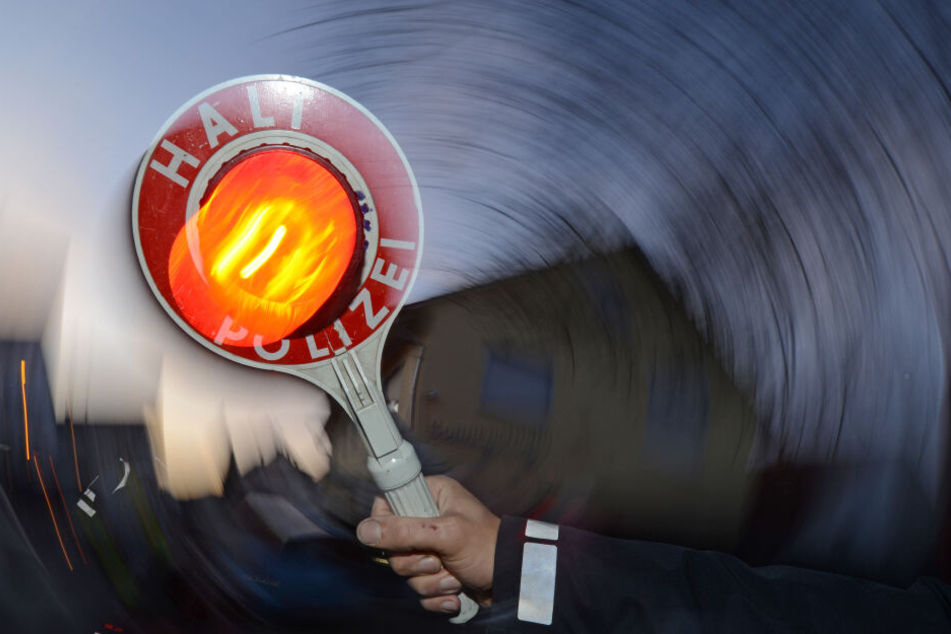 Ein Polizist hält bei einer Verkehrskontrolle eine Kelle mit der Aufschrift "Halt Polizei" hoch (Symbolbild).