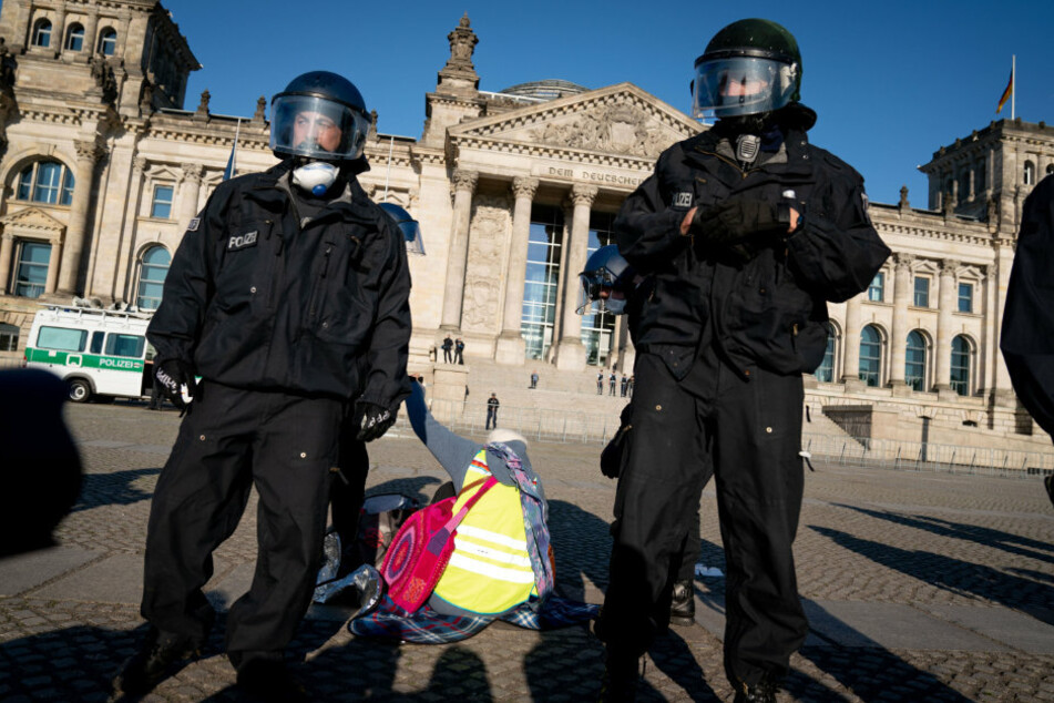 Polizeibeamte mit Helm und Mund-Nasen-Schutz lösen eine Demonstration vor dem Reichstagsgebäude auf.