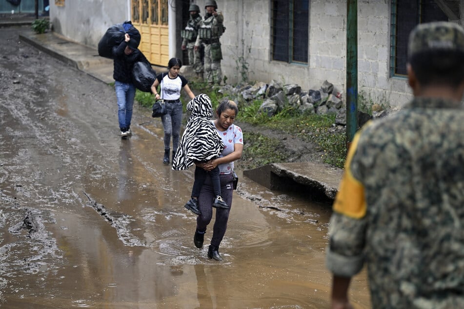 A woman carrying a child wades through a flooded street due to the rains in the municipality of Huauchinango, Puebla State, Mexico, on October 11, 2025.