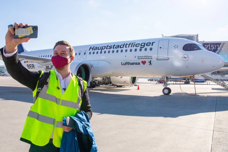 Ein Mann steht vor einem Lufthansa Airbus vom Typ A320neo mit der Aufschrift "Hauptstadtflieger" und macht auf dem Rollfeld des Münchner Flughafens Franz-Josef Strauß ein Seflie.