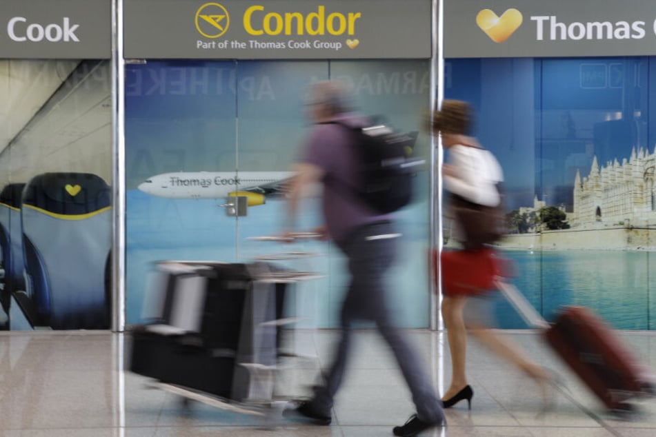 Passagiere gehen an einem Büro von Condor und Thomas Cook am Flughafen Palma de Mallorca vorbei.