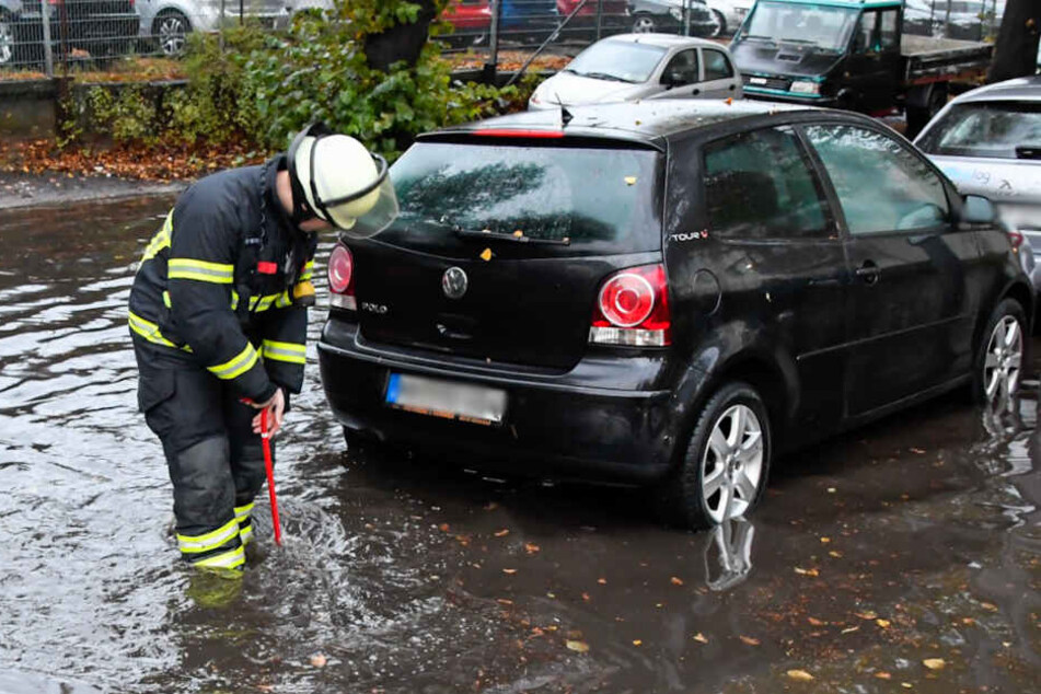 Ein Feuerwehrmann steht knöcheltief im Wasser und versucht den Gulli von Laub zu befreien.