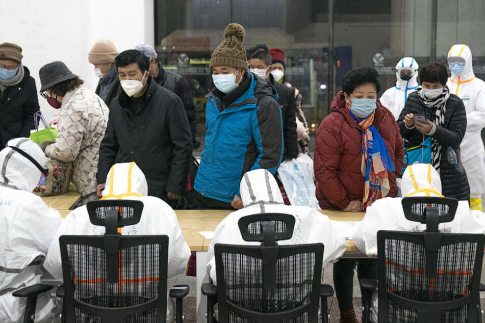 Wuhan: Medizinisches Personal in Schutzanzügen helfen mit dem Coronavirus infizierten Patienten bei ihrer Ankunft in einem Hilfskrankenhaus.