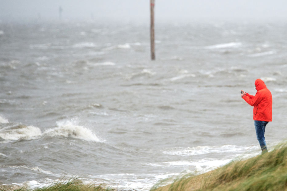 Ein Mann fotografiert an einem Strandabschnitt die peitschenden Wellen der Nordsee.
