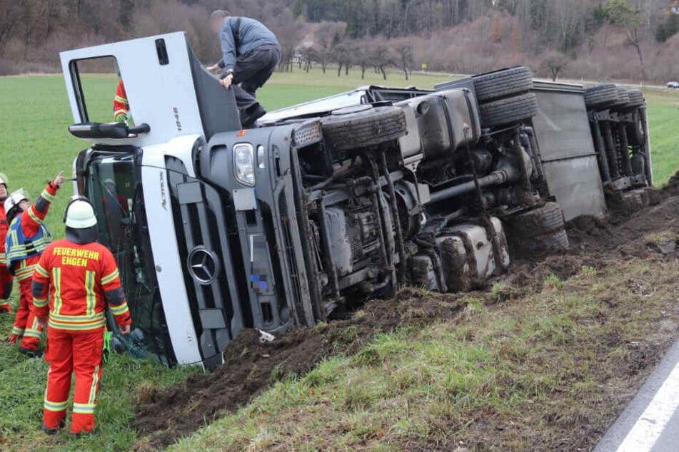 Der Lkw liegt auf der Seite in einer Böschung neben der Straße.