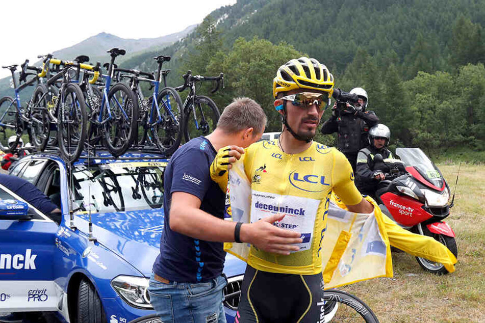 Julian Alaphilippe aus Frankreich vom Team Deceuninck-Quick-Step im gelben Trikot zieht sich vor dem Teamwagen eine Jacke an