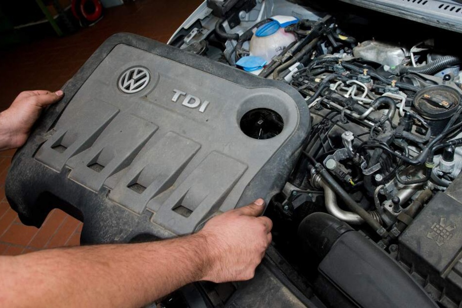 Ein KFZ-Servicetechniker hält die Abdeckung vor einen vom Abgas-Skandal betroffenen 2.0l TDI Dieselmotor vom Typ EA189.