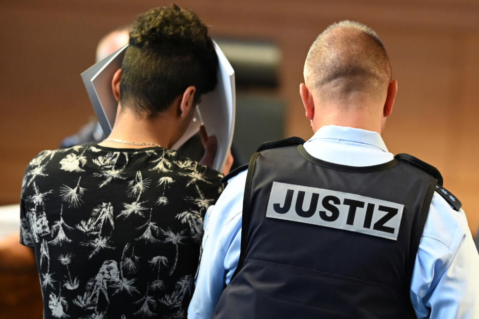 Einer der Angeklagten wird von einem Justizangestellten in den Gerichtssaal gebracht.