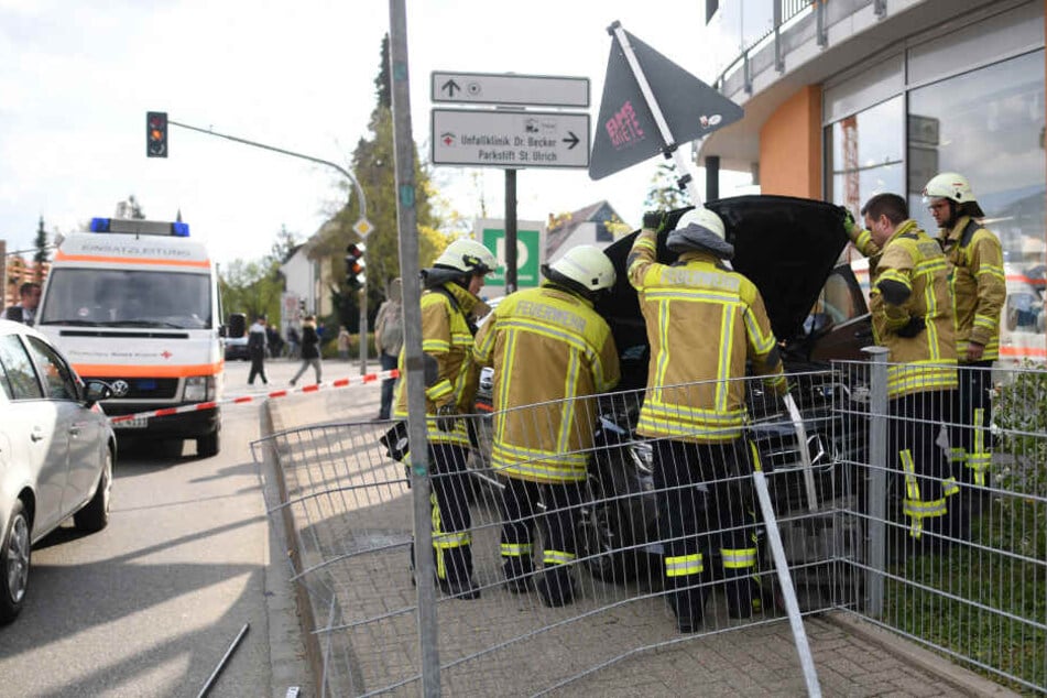 Feuerwehrmänner stehen vor einem Auto am Straßenrand.