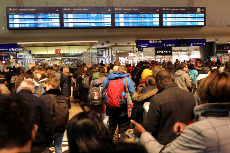 Bahnreisende vor einer Informationstafel.