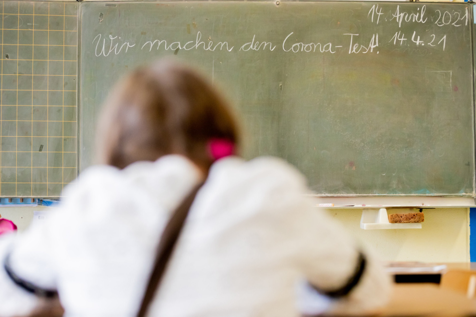 Eine Schülerin sitzt bei einem Probelauf mit Corona-Schnelltests an der Grundschule in der Köllnischen Heide in Berlin-Neukölln vor einer Tafel mit der Aufschrift "Wir machen den Corona-Test".