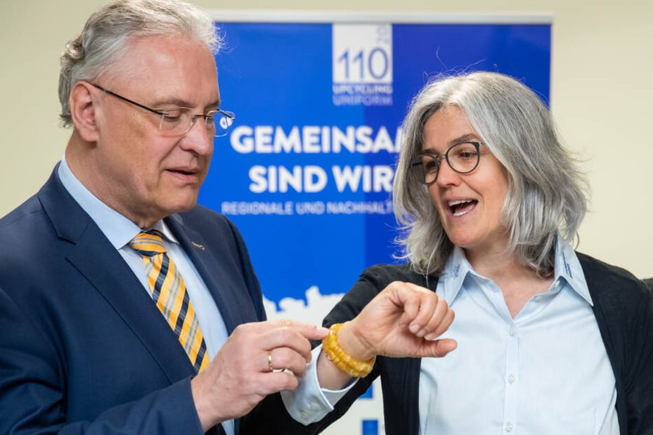 Joachim Herrmann (CSU), Innenminister von Bayern, betrachtet am Hangelenk von Katharina Werner, Projektleiterin für das Upcycling alter Polizeiuniformen bei den Barmherzigen Brüdern, "Knöpfe-Armband" bestehend aus Hemdknöpfen alter Polizeiuniformen.