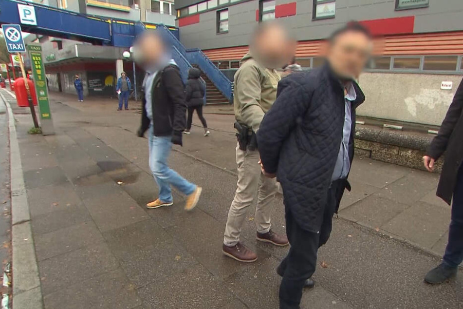 Polizeibeamte führten den Verdächtigen in Handschellen ab.