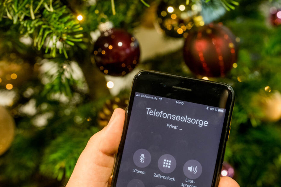 Mit einem Smartphone wird die Nummer der Telefonseelsorge vor einem Weihnachtsbaum gewählt.