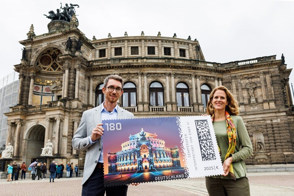 Nora Schmid (r.) und Benjamin Löwen (Vice President Frankierung/Infrastruktur Deutsche Post) präsentieren stolz die neue Briefmarke vor der Semperoper in Dresden.