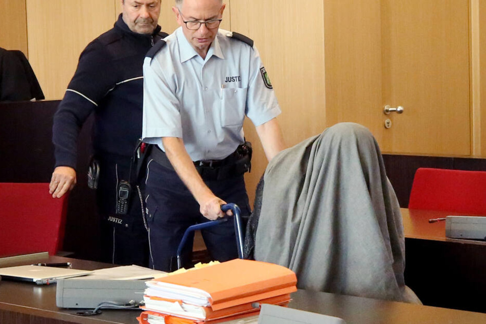Der Angeklagte wird von einem Justizbeamten im Rollstuhl in den Gerichtssaal gefahren.
