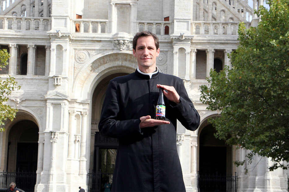 Pfarrer Jeremie Schaub steht mit einer Flasche "Ste Kat" Craft Beer vor "seiner" Kirche.