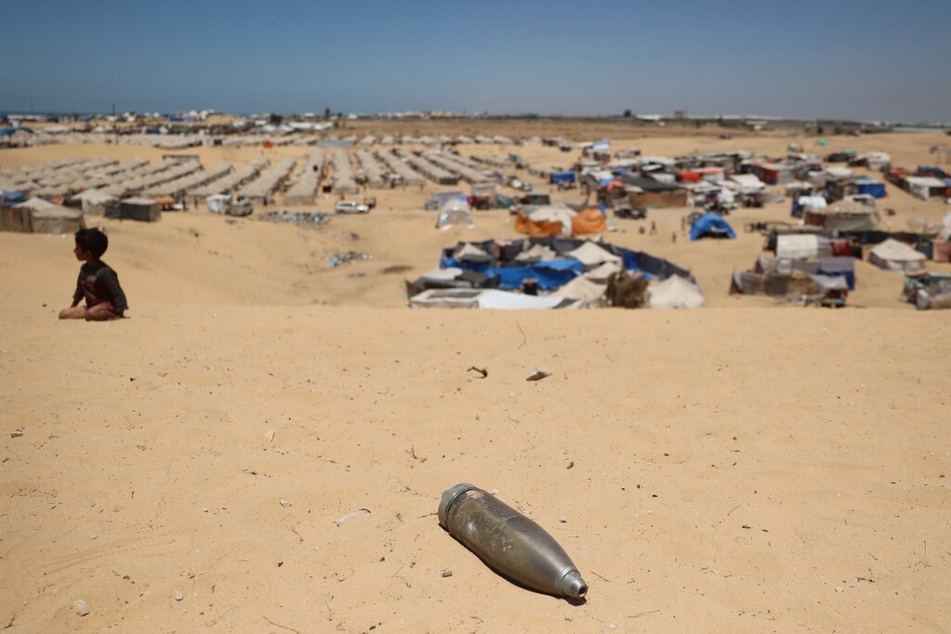 An unexploded shell lies on a sand dune as a young boy sits near a makeshift camp for displaced Palestinians in the area of Tal al-Sultan in Rafah in the southern Gaza Strip.