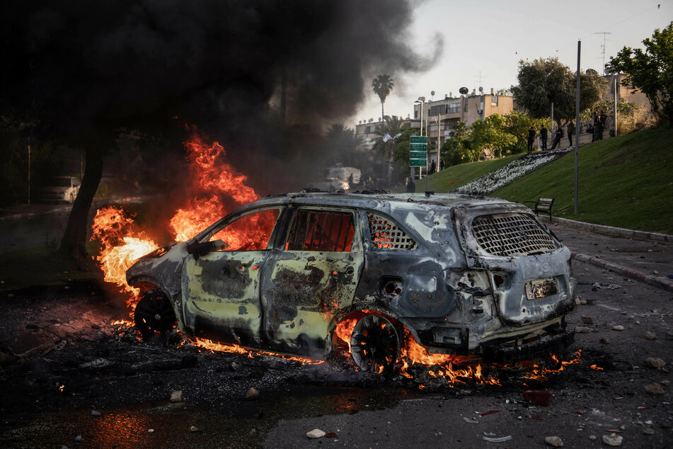 Das Wrack eines Autos steht brennend auf einer Straße in Lod. In der Stadt kam es zwischen israelischen Sicherheitsbeamten und israelisch-arabischen Demonstranten zu Zusammenstößen.