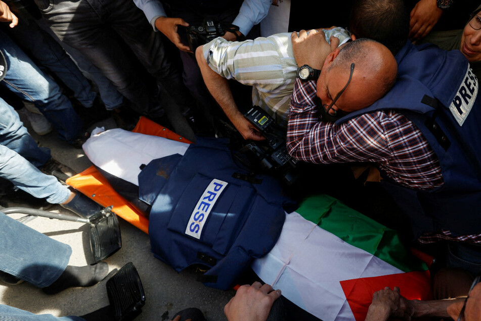 Colleagues of Shireen Abu Akleh grieve over her coffin.