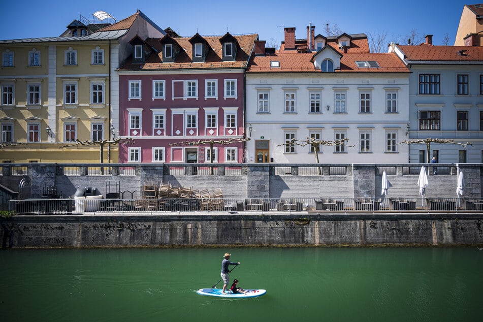 Ein Stehpaddler fährt mit einem Board, auf dem außerdem ein Junge sitzt, über die Ljubljanica in Slowenien.