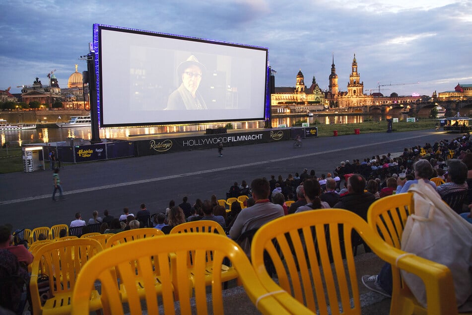 Zahlreiche Gäste der "Filmnächte am Elbufer" sitzen vor der Kulisse der Dresdner Altstadt und schauen auf eine Kinoleinwand. Das Freiluftkino startete am Donnerstag auch in Zeiten des Coronavirus mit dem Film "Bohemian Rhapsody".