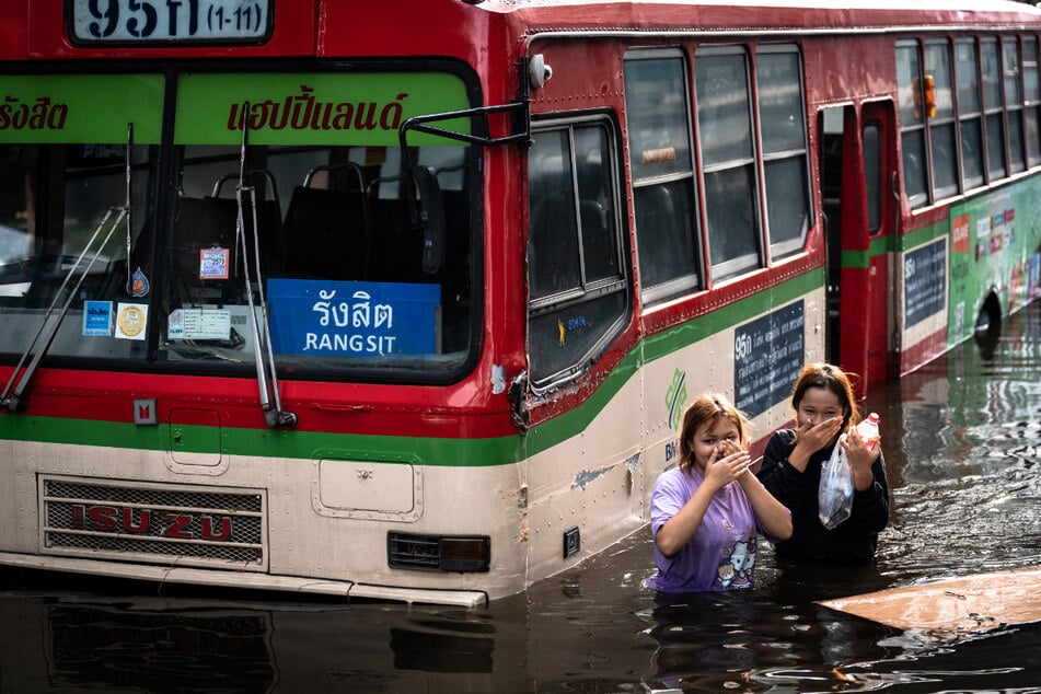 Frauen gehen im Stadtteil Bang Kapi in Bangkok an einem verlassenen Bus vorbei.