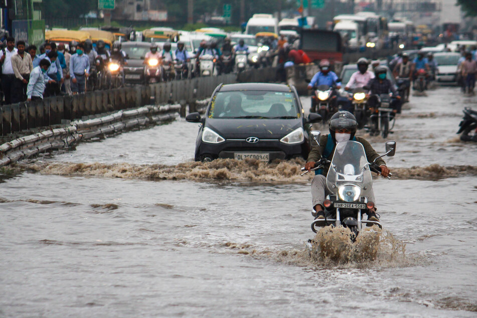 Pendler bahnen sich ihren Weg durch eine überflutete Straße nach starken Regenfällen in Indien. Mehrere Menschen sind gestorben.