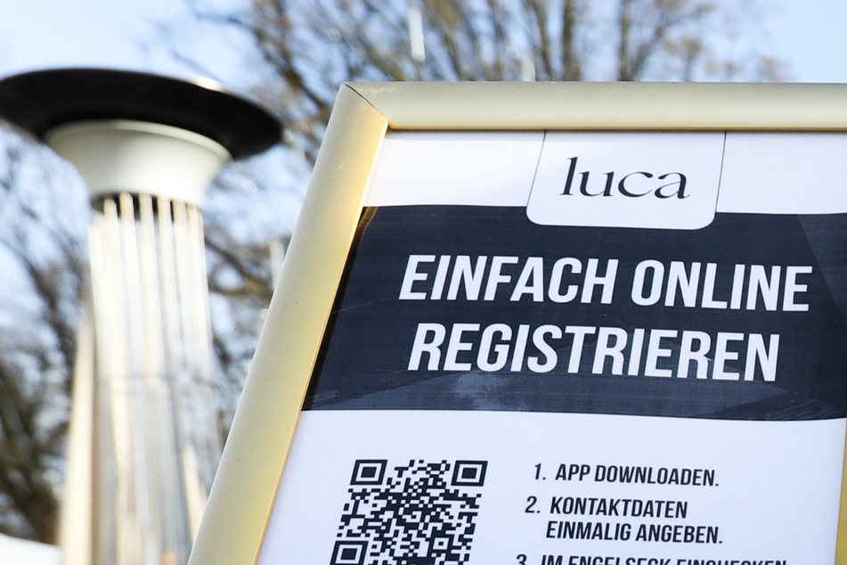 12.04.2021, Schleswig-Holstein, Timmendorfer Strand: Ein Hinweisschild zur Nutzung der Luca-App ist am Eingang zu einem Cafe zu sehen. Hamburg hat eine Lizenz für die Nutzung des Luca-Systems einschließlich der Luca-App zur Nachverfolgung von Corona-Kontakten erworben. Foto: Christian Charisius/dpa +++ dpa-Bildfunk +++