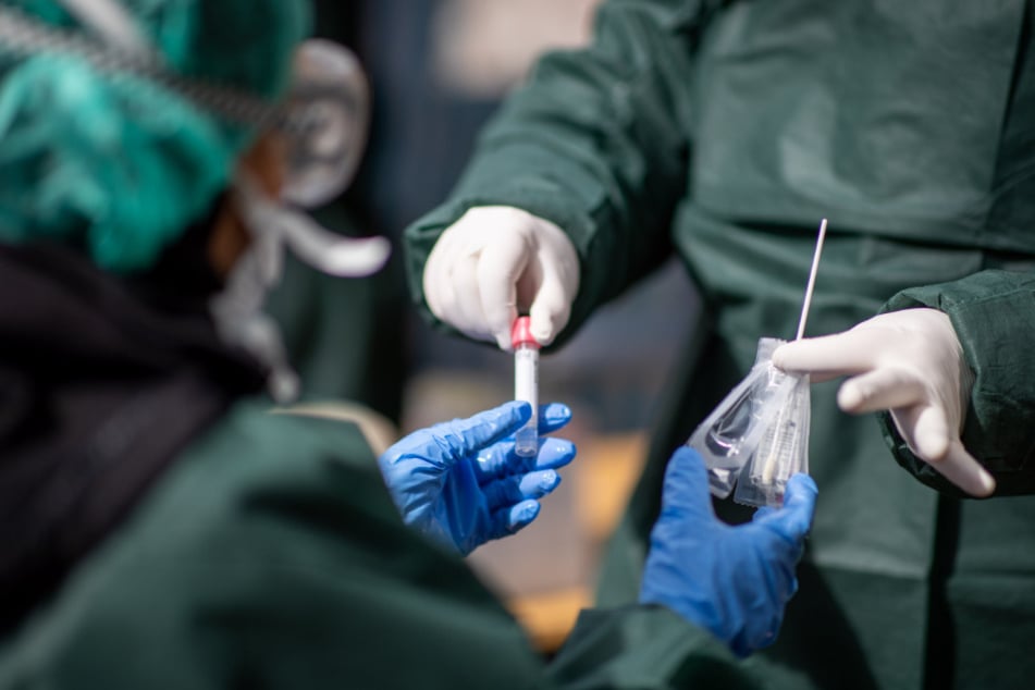 Eine Mitarbeiterin des Gesundheitsamtes übergibt ihre Kollegin in einem Corona Testzentrum ein Abstrichtupfer mit Röhrchen.