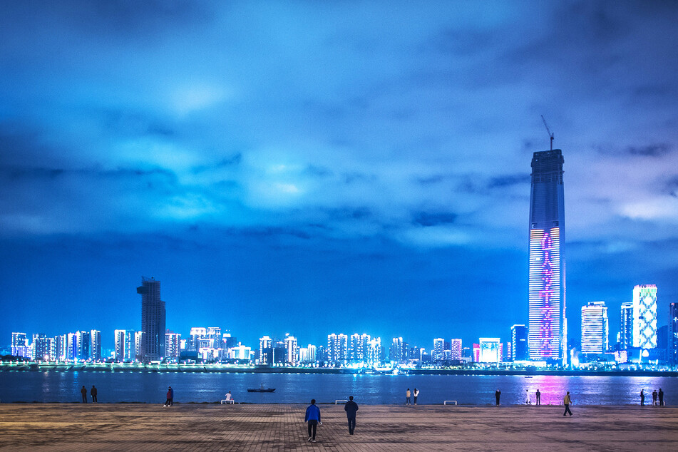 Bürger stehen im Hankou Jiangtan-Park von Wuhan am Ufer und betrachten die Skyline eines Stadtteils.
