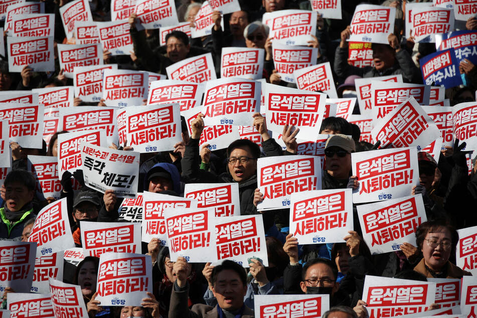 Protesters raise signs that read "Step down President Yoon Suk Yeol" as people and lawmakers attend a rally to condemn the surprise martial law declaration, at the National Assembly in Seoul on December 4, 2024.