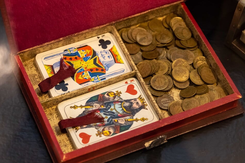 Historische Karten und Spielgeld liegen in einer Holzschatulle.