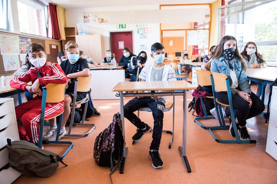 Schüler einer 7. Klasse der Max-Schmeling-Stadtteilschule sitzen zu Beginn des Unterrichts mit Mund-Nasen-Bedeckungen im Klassenraum.