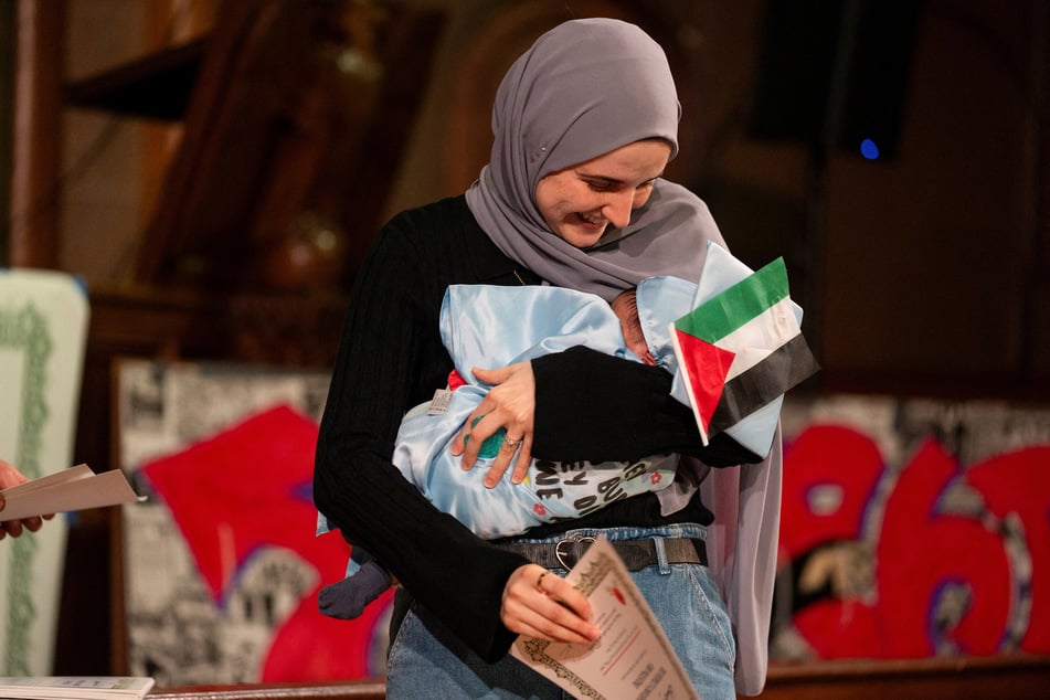 Dr. Noor Abdalla accepts an honorary diploma for her husband, Mahmoud Khalil, while holding their one-month-old baby at the People's Graduation at the Cathedral of St. John the Divine in New York City on May 18, 2025.