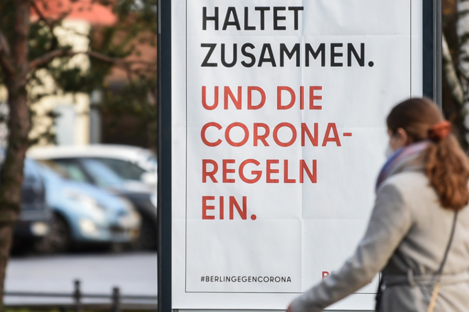 Auf dem Gehweg steht ein Schild mit der Aufschrift "Haltet zusammen. Und die Corona-Regeln ein."