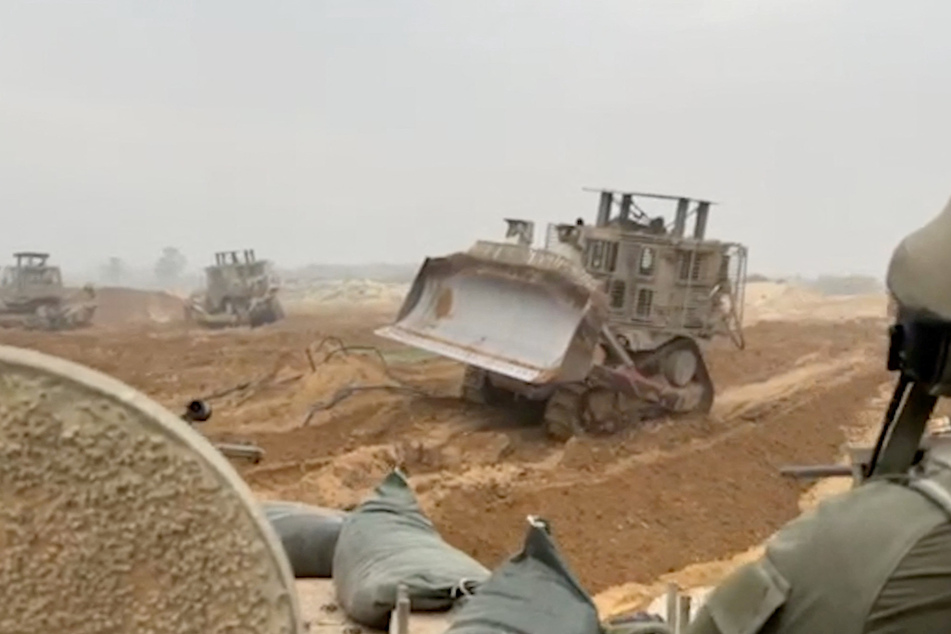 An Israel Defense Forces armored vehicle waits as armored bulldozers clear path in a location given as Gaza.