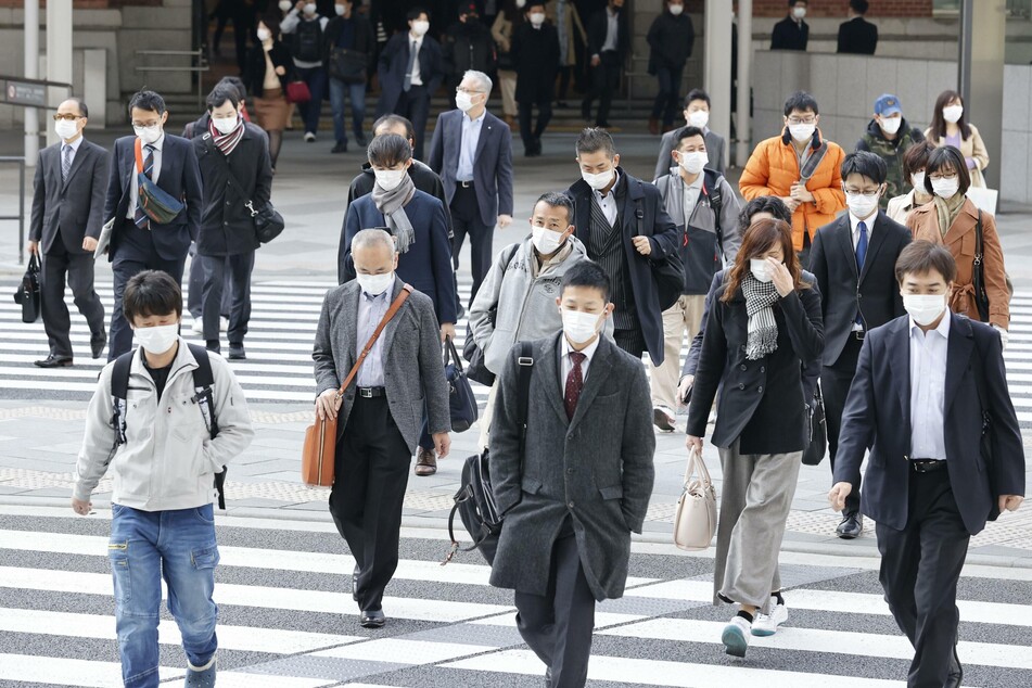 Pendler mit Mundschutz gehen im Geschäftsviertel Marunouchi in Tokio über eine Straße.