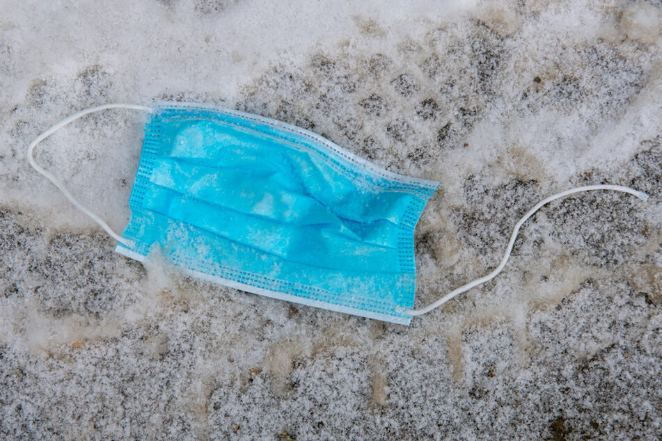 Ein getragener, einfacher Mund-Nasen-Schutz liegt auf dem Gehweg im Schnee.