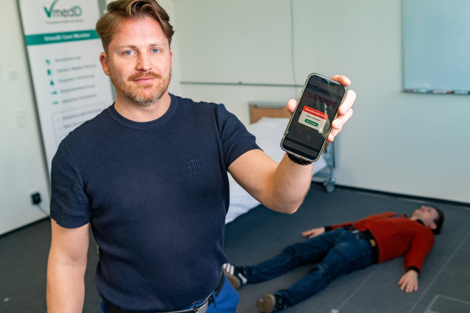 Entwickler Sebastian Hauschild (44) zeigt die Warnmeldung auf dem Handy. Sein Kollege Paul Ebert (35) simuliert einen gestürzten Menschen.