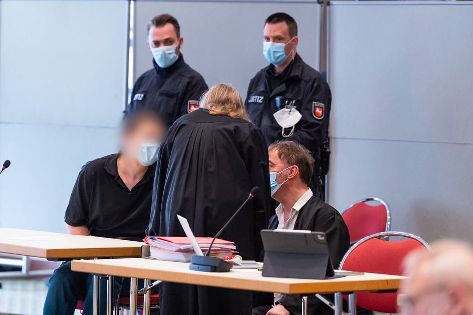 Der Angeklagte (l) spricht mit seinen Verteidigern im Gerichtssaal.