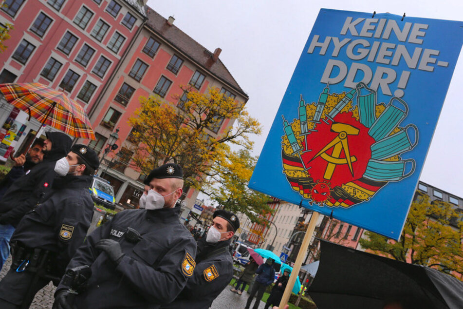 Polizisten stehen auf dem Gärtnerplatz bei einer Demonstration gegen die Corona-Maßnahmen neben den Demonstranten, die u.a. ein Schild "Keine Hygiene-DDR!" mit sich führen.