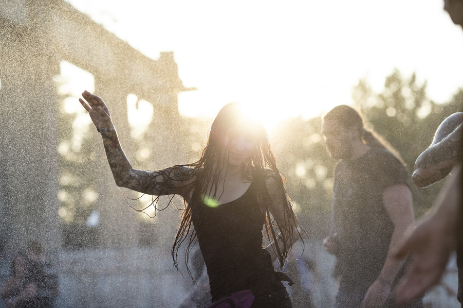 Eine Besucherin tanzt im Sonnenuntergang bei 30°C im Wassernebel auf dem Full Force Festival in Ferropolis.