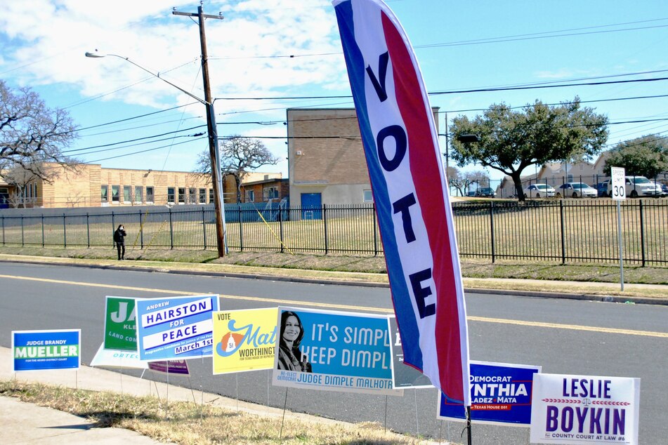 A polling place in East Austin boasts a tall "VOTE" flag and several campaign signs near the street.