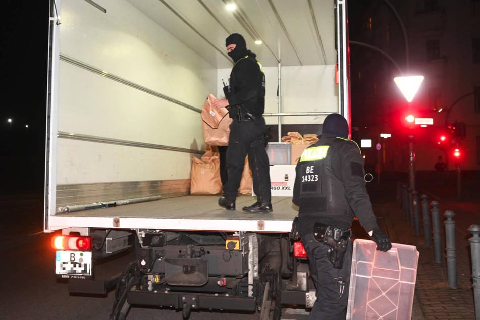 Zwei Polizisten verladen die beschlagnahmten Beweismittel auf einen Laster.