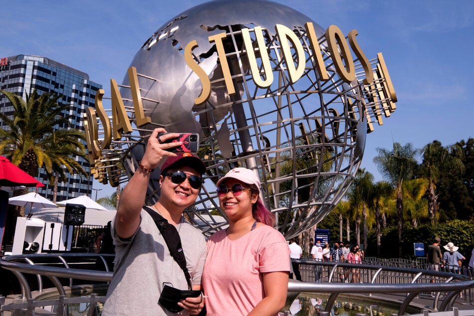 Ein Paar fotografiert sich vor dem Schriftzug Universal Studios Hollywood auf einer Weltkugel-Skulptur. Am Dienstag hob Kalifornien die meisten seiner Covid-19-Beschränkungen auf.